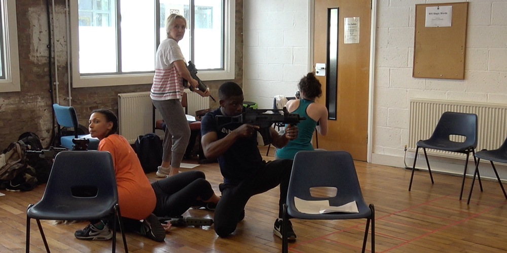 Actors practicing with machine guns in a rehearsal room